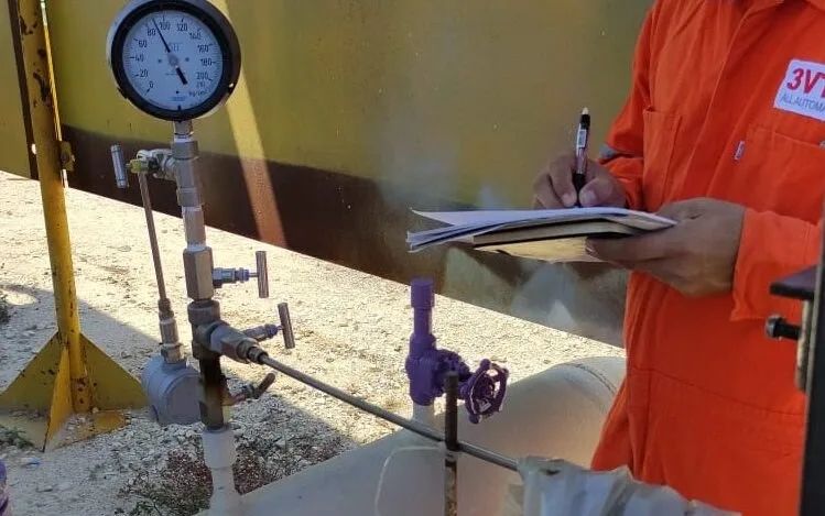 Operador industrial midiendo presión en planta de automatización y control de procesos, válvulas y manómetro en entorno de producción.